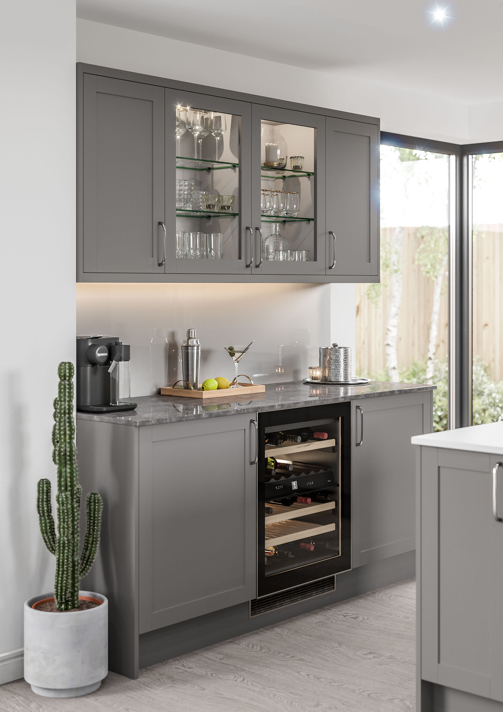 Skye Shaker Kitchen in dust grey is shown in this kitchen design. White worktops and dust grey cabinets create a modern kitchen feel. A mix of tall cabinets and larders along with a kitchen island, creates an impressive space. Wall to ceiling windows make the kitchen bright and airy, there are also smart features like a coffee machine, designer bar stools and cooker with hood in matte black.