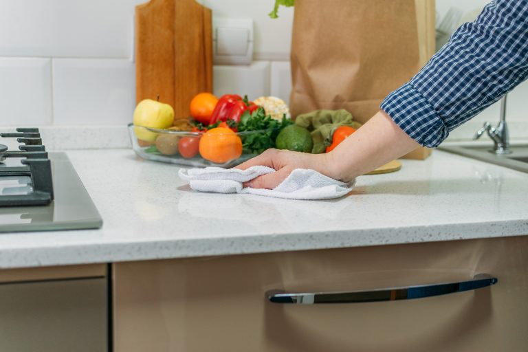 Hand wiping kitchen worktop with fruit and vegetables