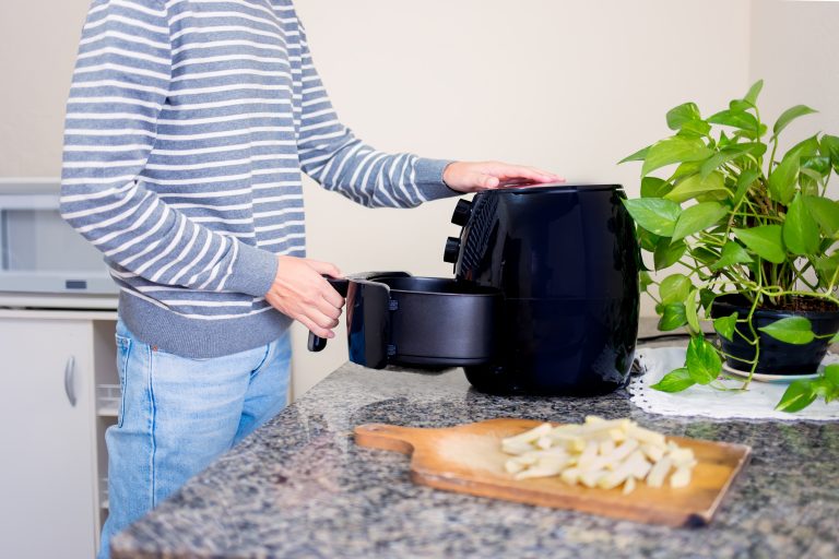 Man using an air fryer to cook sliced potatoes